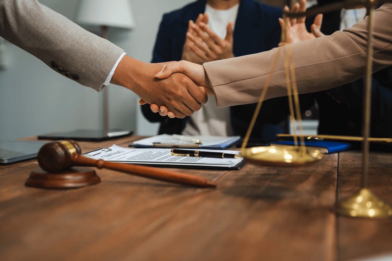 Two people in business attire shaking hands across a desk with legal documents